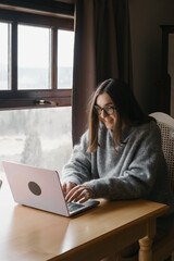 Woman content creator using a laptop. Female in cozy sweater smiling and consulting on-line. Remote work, study, SMM, UGC