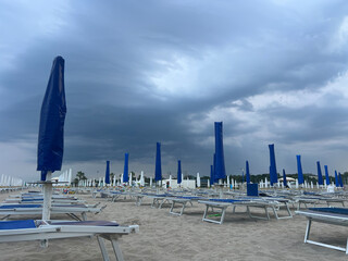 Closed blue umbrellas on deserted beach under stormy sky