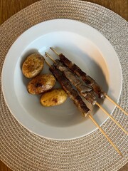 Grilled meat skewers with roasted potatoes on a white plate
