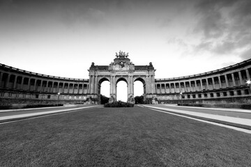 Obraz premium Brussels Belgium, panoramic black-and-white view of the Cinquantenaire triumphal arch and colonnades at dawn, empty park lawn in foreground, neoclassical landmark, travel architecture background.