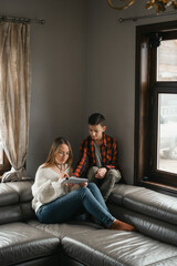 Teenager with mother playing on console at home. Woman and son sitting close together on leather couch in a relaxed, indoor setting.