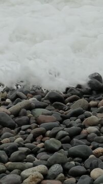 The stormy sky over the rocky seashore on pubble beach with smooth round stones. Waves washing stones on coastline. Slow motion cinematic close up shot. Zen and tranquility concept