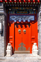 Traditional Chinese red wooden door with lion head knockers and stone guardian lions. Beijing, China.