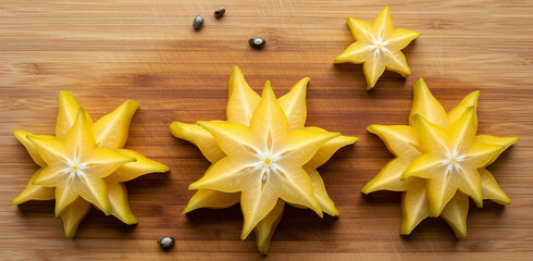 Fototapeta premium Overhead view of fresh peeled starfruit slices artistically arranged in floral shapes on a rustic wooden cutting board. The natural pattern and bright color of the fruit create a visually appealing 