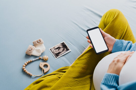 Pregnant woman with smartphone. Closeup pregnant belly with ultrasound photo and medical notes.