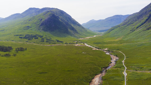 Aerial view of lush green valley nestling between towering mountains, river snaking through the landscape, creating a vibrant tapestry of nature's artistry, Glencoe, Scotland, United Kingdom.