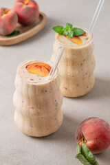 Two glasses of smoothie with peach and banana on a light background with tropical fruits.