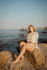 beautiful young girl with a beautiful athletic figure of European appearance in a swimsuit and underwear on the ocean shore in the open air. Sea waves and rocks with blue water. Travel and recreation