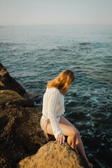 beautiful young girl with a beautiful athletic figure of European appearance in a swimsuit and underwear on the ocean shore in the open air. Sea waves and rocks with blue water. Travel and recreation