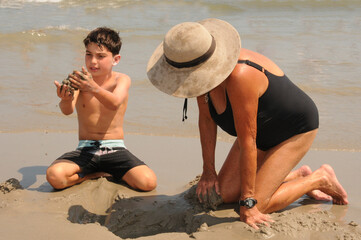 Grandmother and grandson playing in the sand on the beach during the summer at the shore.