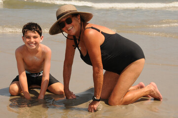 Grandmother and grandson playing in the sand on the beach during the summer at the shore. Both are smiling and looking at the camera.