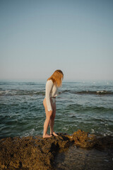 beautiful young girl with a beautiful athletic figure of European appearance in a swimsuit and underwear on the ocean shore in the open air. Sea waves and rocks with blue water. Travel and recreation