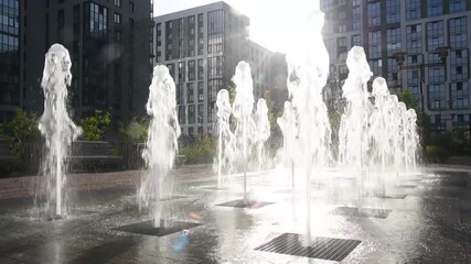 fountain of clean water in courtyard of residential complex, numerous jets of water, multi-storey buildings in background, bright sunshine, landscaping of city - Powered by Adobe