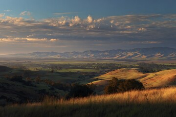 Scenic Landscape of Rolling Hills and Mountain Range Under Dramatic Sky During Sunset