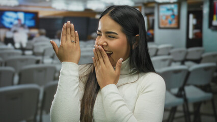 Woman holds ring showing excitement in a gallery art exhibit as a young latin hispanic observer admires outdoor engagement moment.