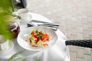 Elegant brunch scene with eggs benedict and smoked salmon, garnished with greens and sauce, served with coffee on a bright, stylish table setting.