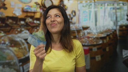 Woman with visible hands holding and fanning chile pesos banknotes in sweet shop counting bills;...