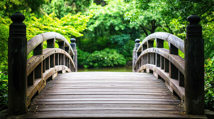 Fototapeta premium A wooden bridge with curved arches spans a tranquil pond in a lush, green garden. The bridge is adorned with ornate wooden posts and railings