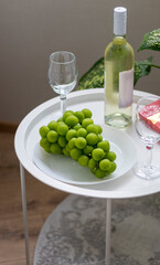 Bottle of white wine, large grapes, box of chocolates, wine glasses on the small coffee table. Celebration