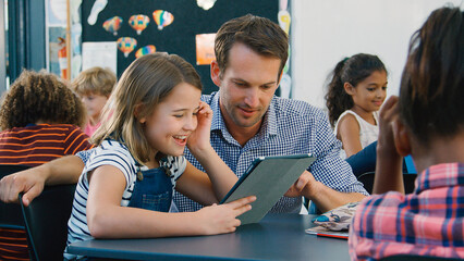 Male High School Teacher With Female Pupil Using Digital Tablet At Desk In Technology Class