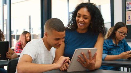 Female High School Teacher With Male Pupil Using Digital Tablet At Desk In Technology Class