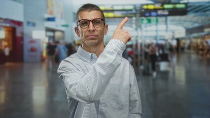 Fototapeta premium Man pointing in busy airport with people blurred in background suggesting travel, confusion for navigating terminal