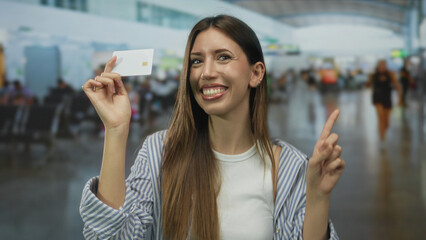 Young smiling hispanic woman pointing finger to creditcard at airport terminal; travel confidence...