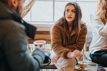 A woman, seated at a coffee shop, attentively listens and stirs her coffee, surrounded by a warm and friendly atmosphere.