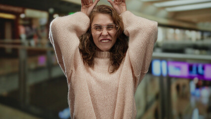 Woman expressing surprise indoors at a mall with her hands on head wearing glasses and a sweater...