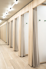 Well-lit row of dressing rooms for trying on clothes in a shop with wooden frames and textile curtains in a modern and sustainable clothing store