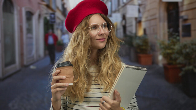 Woman sips coffee before holding her pad on street as she reveals a sketchbook in front of onlookers, blonde young student wearing glasses appearing pensive during an outdoor workshop.