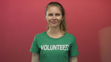 Fototapeta premium Woman uses hands adjusting volunteer glove and plastic wrap over green shirt while her blonde hair frames a gentle smile in an indoor setting.
