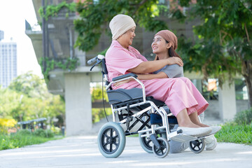 Asian careful caregiver or nurse and woman with cancer is sitting in a wheelchair. in the garden. Concept of happy retirement with care from a caregiver and Savings and senior health insurance.