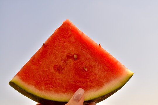 Hand holding a watermelon slice up to the sky on a bright sunny day. Summer, joy, and healthy nutrition.

