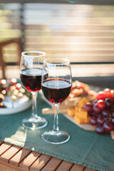 Red wine glasses and assorted aperitivo snacks on wooden plate on a sunny garden party table.