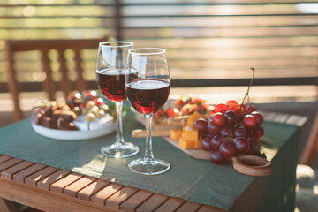 Red wine glasses, bruschettas with tomatoes, salami and basil, bread, Camembert cheese, grapes. Summertime, rooftop dating concept. Home party concept.