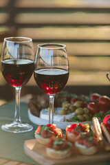 Red wine glasses and assorted aperitivo snacks on wooden plate on a sunny garden party table.