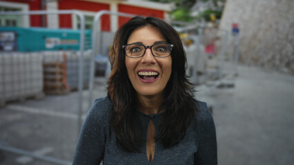 Fototapeta premium Woman smiling with glasses and patterned blue blouse at construction site surrounded by scaffolding and machinery; unexpected surprise.