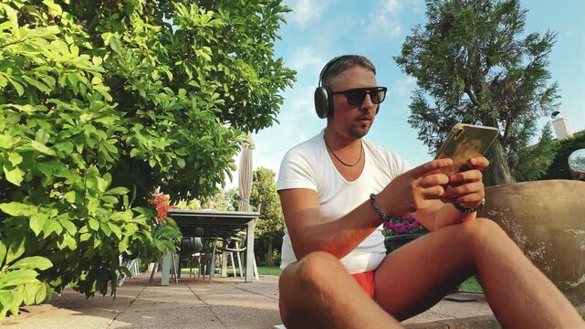 Man seated outdoors with tablet and headphones at golden hour