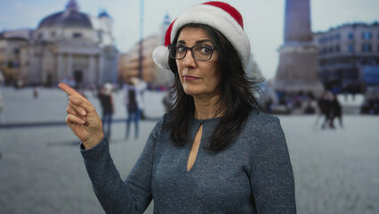 Woman wearing a red santa hat points her finger at the viewer beside a building facade in vatican...