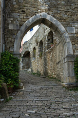 Historic stone street climbing uphill through arched passage in old medieval wall in Motovun, Istria, Croatia. Charming European townscape perfect for travel, history, architecture themes.