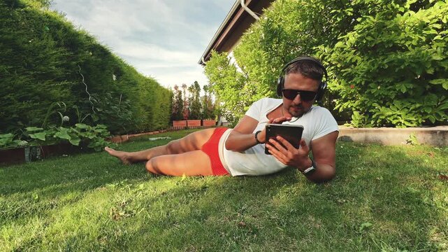 Man lying on grass reading tablet outdoors
