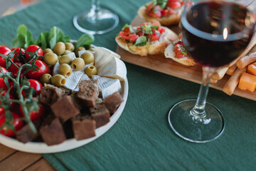 Close-up of a plate with assorted snacks and glasses of red wine on a terrace table in the summer.