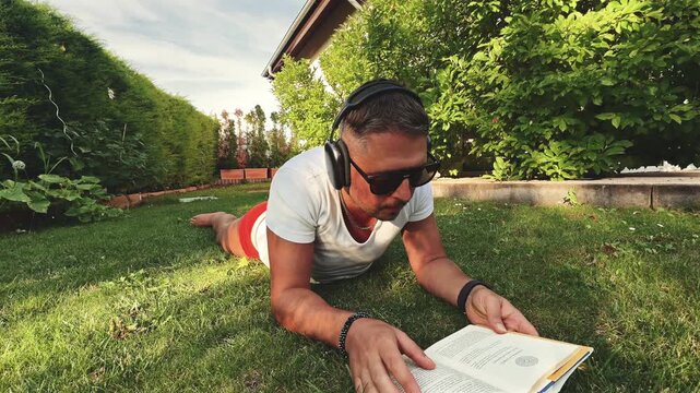 Man lying on garden lawn reading a book during golden hour