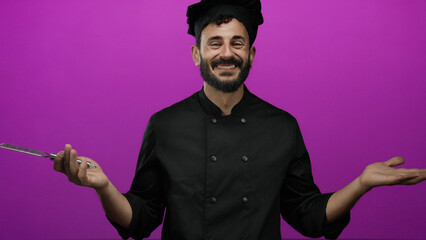 Hispanic man chef with beard in black uniform holding cheese grater against vibrant pink background smiling confidently.