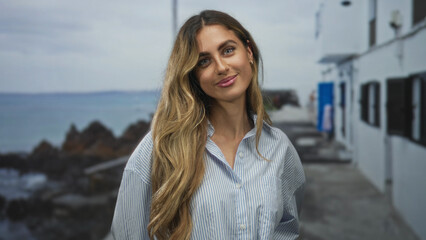 Obraz premium Woman shows smiling face and slight head tilt on seaside walkway near coastal buildings; joy calm contentment relaxation.