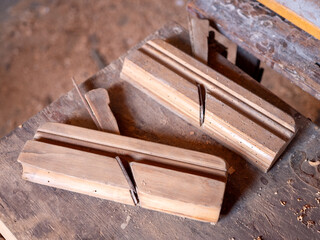 Two old wooden molding planes on a dusty carpenter workbench in a traditional woodworking shop, used for manual profiling of wooden strips.