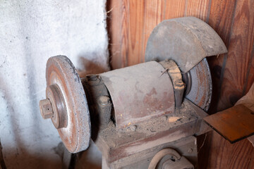 Old dusty bench grinder in a wooden workshop. The vintage sharpening machine shows signs of use and age, capturing a rural and practical workshop environment.