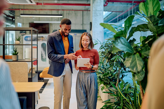 Two businesspeople using tablet, collaborating in modern green office space, discussing project, sharing ideas, teamwork, communication, technology, innovation, startup