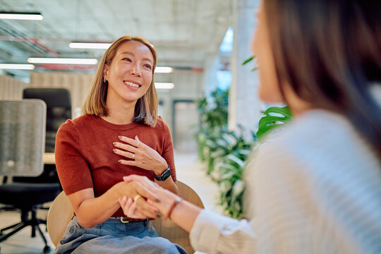Two asian businesswomen shaking hands during a meeting in a modern office, showing respect and partnership